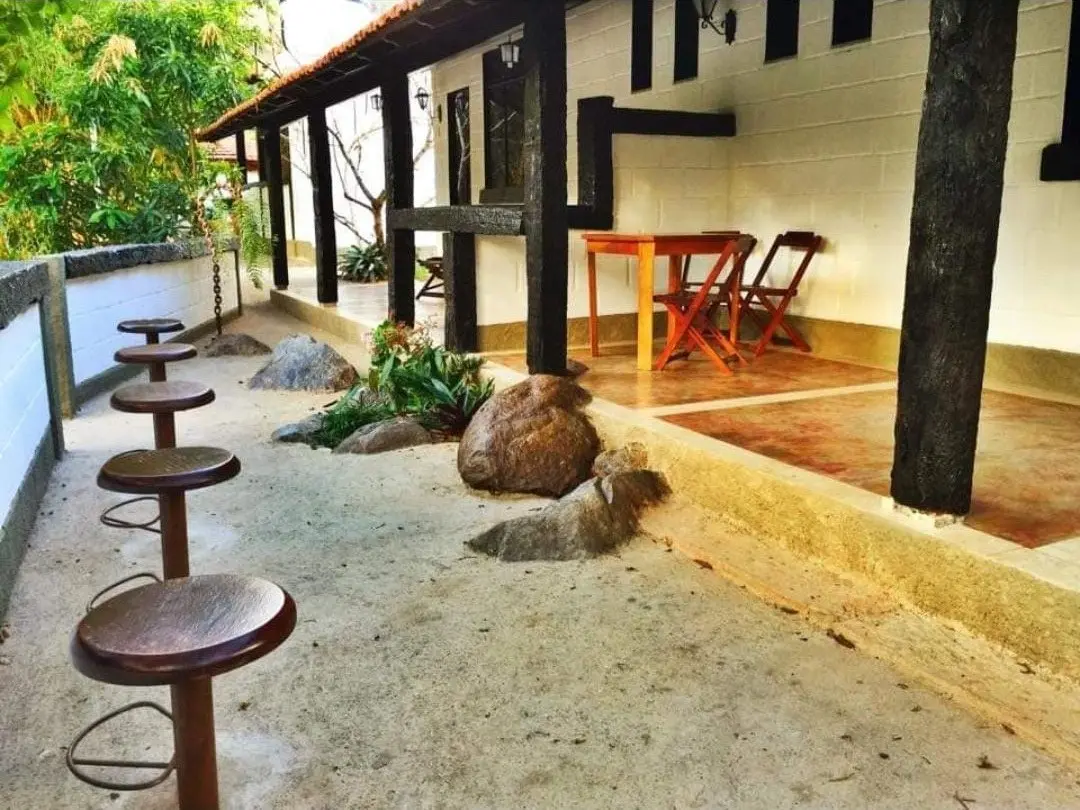 Varanda com pilares de madeira, jardim de pedras e banquetas voltadas para o verde