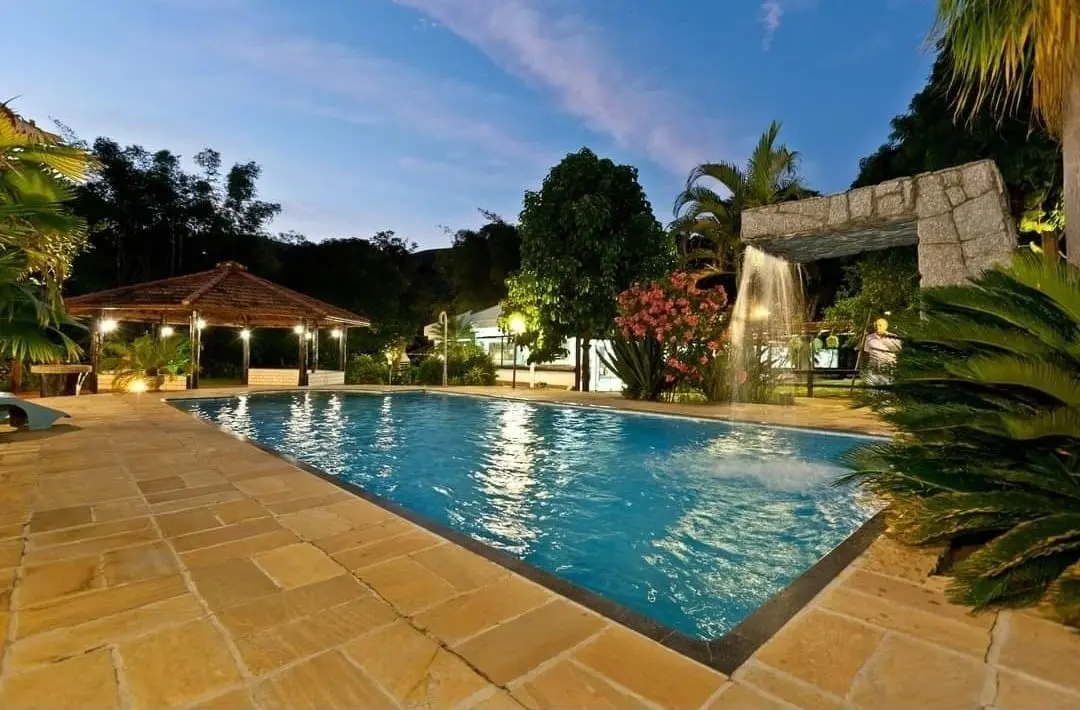 Piscina ao entardecer, com quiosque coberto e vegetação ao redor