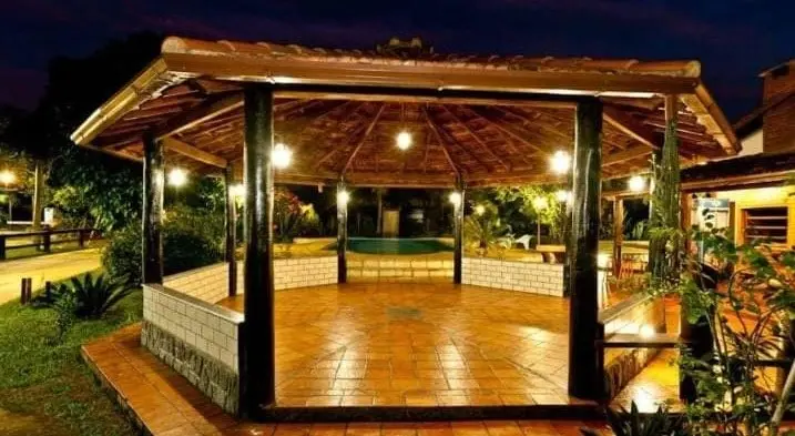 Quiosque de madeira iluminado ao anoitecer, com deck e gramado ao redor