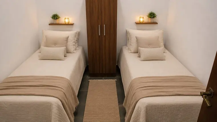 Quarto com duas camas de solteiro, roupa de cama clara e armário de madeira