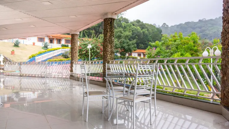 Varanda envidraçada com mesas e cadeiras, voltada para a serra