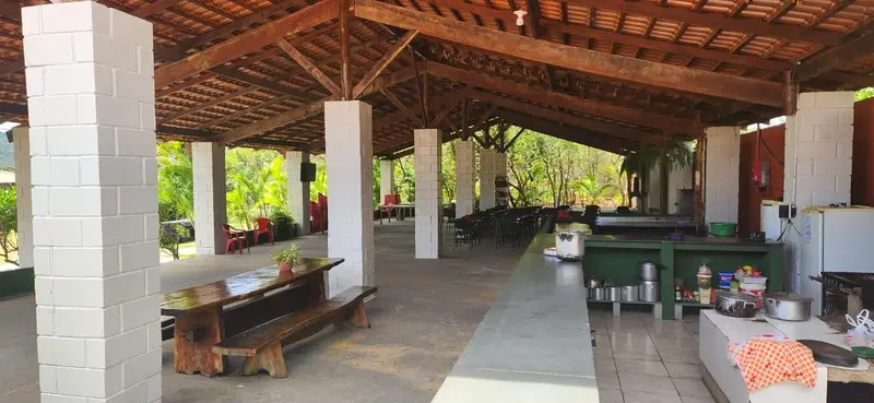 Salão coberto com mesas de madeira e área de cozinha