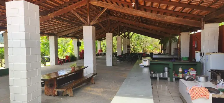 Salão coberto com mesas de madeira, bancada e área de cozinha