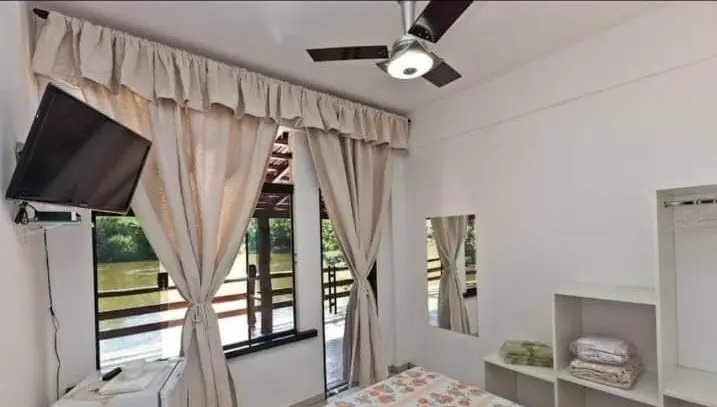 Quarto com cama de casal, televisão e cortinas claras