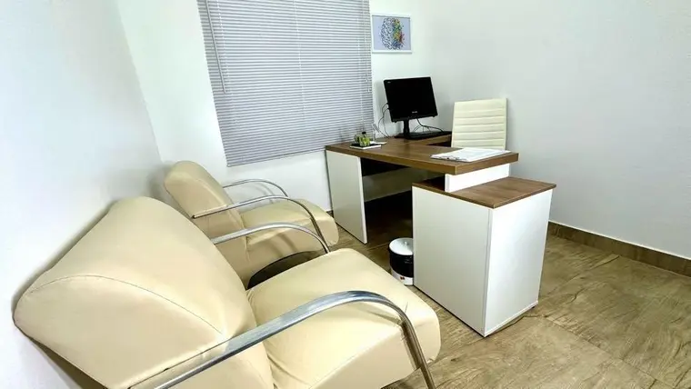 Sala de atendimento com poltronas, mesa de trabalho e janela ampla