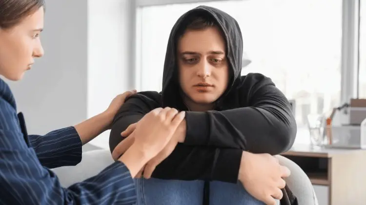 Mulher amparando outra sentada com os braços em volta dos joelhos