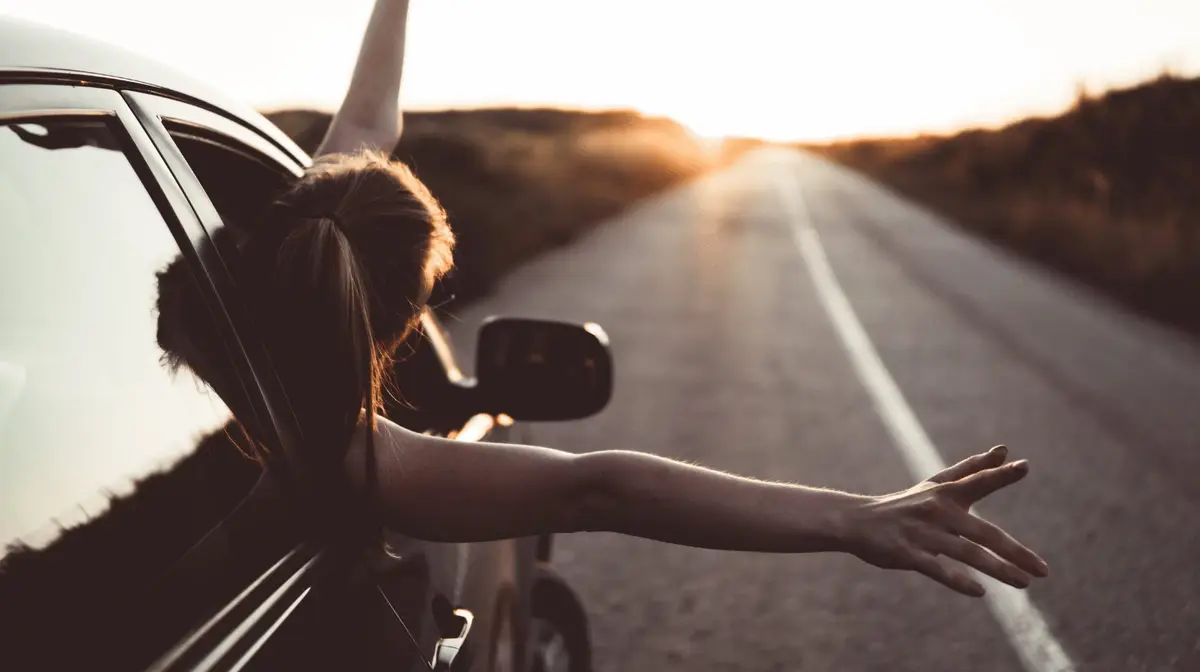 Braço para fora da janela de um carro em uma estrada ao entardecer