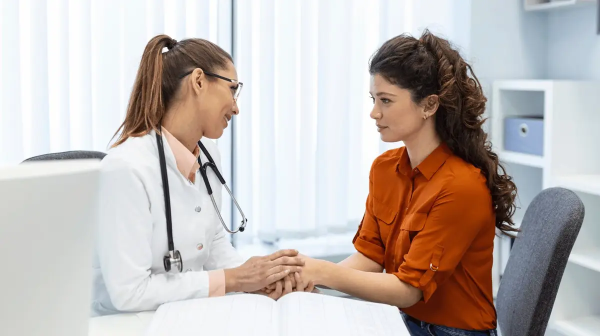 Profissional de saúde segurando as mãos de uma mulher durante uma consulta