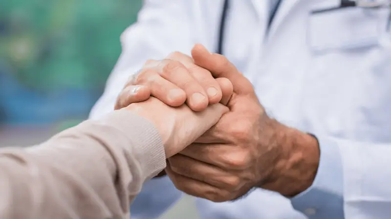 Profissional de saúde segurando com as duas mãos a mão de uma pessoa idosa