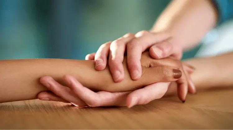 Mãos de várias pessoas sobrepostas sobre uma mesa, em sinal de apoio