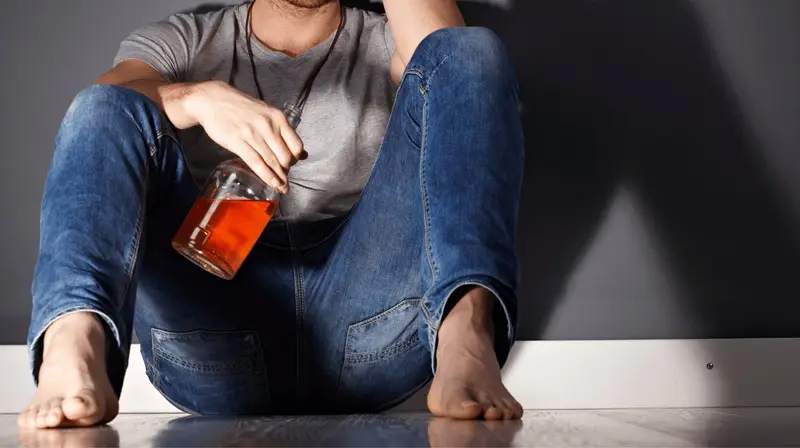 Pessoa sentada no chão, encostada na parede, segurando uma garrafa